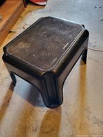 Overall view of black molded plastic step stool showing textured top and condition