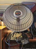 Front view of Presto HeatDish Plus Tilt parabolic heater showing reflector, wire guard, center element, stand, and power cord