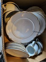 Box contents showing stack of small plates, larger plates, and cups with matching gold trim