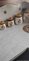 Four graduated mushroom motif ceramic canisters on countertop