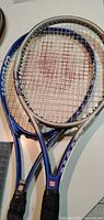 Two blue/silver Wilson rackets showing string condition and grip tape wear