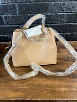 Front view showing tote, top handles, detachable strap wrapped in plastic