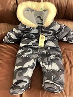 Front view of blue dinosaur print George snowsuit showing zipper, hood with faux fur, attached feet and hang tag