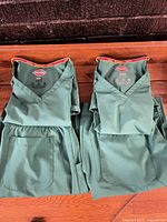 Two folded scrub sets (tops and pants) displayed on wooden surface