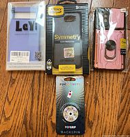 Front view of four packaged items: OtterBox Symmetry case, LeYi Pixel 6a case, pink ring case, PopSockets PopGrip