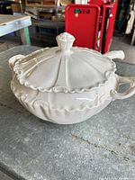 Side view of white ceramic soup tureen with lid and ladle showing overall shape