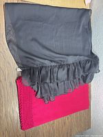 Both scarves laid flat: black chiffon ruffle scarf on top of magenta knit scarf showing fabric textures and colors