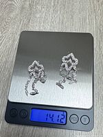 Both earrings on scale displaying 14.12 g