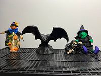 Front view of scarecrow figure, bat statue, witch with skeleton