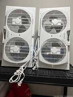 Front view of two identical twin window fans upright showing grills and cords