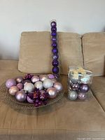 All items on couch: loose ornaments on charger, tube of purple bulbs, cube of mixed bulbs