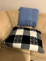 Black & white plaid blanket folded on sofa with blue knit throw draped above