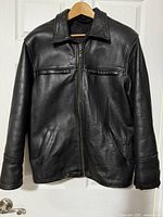 Front view of black leather jacket hanging on hanger