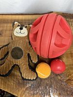All four dog toys displayed: brown corduroy bear plush, large red rubber grooved ball, small orange tennis-style ball, small red rubber ball
