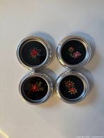Top view of all four coasters showing floral needlepoint designs and silver beaded rims