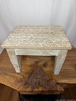 Angled view of small solid wood stool with carved leaf motif top