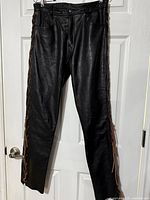 Front view of black leather lace-up pants hanging on door