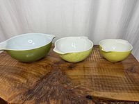 Three nested Pyrex Verde Cinderella bowls on wood surface