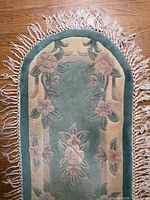 Close view of one end showing floral motif, green field, tan border and fringe