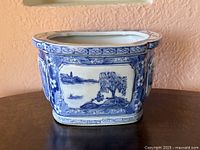 Front view of blue and white porcelain bonsai planter showing landscape panel and floral border