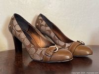 Side view of both Coach heels showing cap toe, buckle strap, and stacked heel