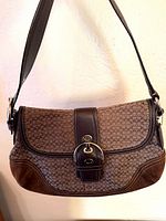Front view of brown Coach Soho signature canvas shoulder bag with leather strap and buckle flap