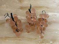 Three pink glass grape clusters on marble surface