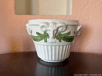 Front view of ceramic cachepot showing ram head and green garland detail