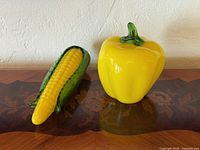 Yellow bell pepper and corn glass sculptures on wood surface