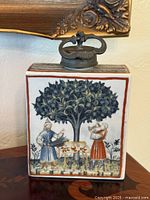 front view of porcelain decanter with tree and figures scene, pewter lid visible