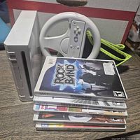 Console standing vertical next to Wii Wheel with remote and stack of five game cases