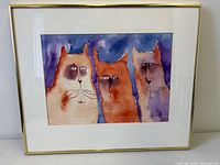 Frontal view of framed watercolour showing three cats, mat and gold frame