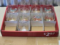 Top view of nine stemless wine glasses in cardboard display tray showing assorted holiday designs
