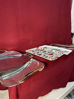 Stacked stainless and glass trays plus melamine floral tray leaning against backdrop