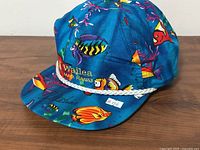 Front/side view of blue ball cap showing tropical fish print, Wailea Maui Hawaii text, white rope detail
