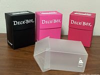 Four Ultra Pro deck boxes—black, two pink, one clear—displayed on tabletop