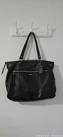 Front view of black Coach leather tote showing exterior zip pocket, straps, hangtag