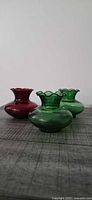 Front angled view of three glass bud vases—two green, one red—showing shape and colour