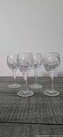 Front view of four pressed-cut cordial glasses standing on wood surface
