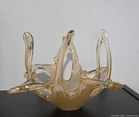 Side profile of amber freeform art glass bowl showing elongated arms and overall shape