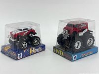 Front view of both sealed mini monster trucks in display cases
