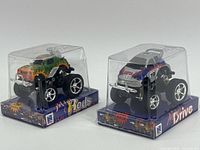 Front three-quarter view of both sealed New-Ray monster truck toys in display cases