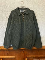 Full front view of dark green Denver cable knit sweater on hanger