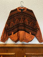 Front view of orange and black hand-woven Ixil Nebaj jacket on hanger