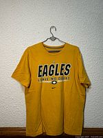 Front view of yellow Nike Eagles T-shirt hanging, showing graphic and overall condition
