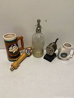All five items upright: tap handle, seltzer bottle, pencil sharpener, stein, mug