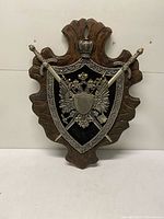 Full view of plaque showing wood backing, metal crest, crossed swords