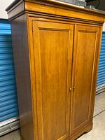 front three-quarter view of armoire showing crown molding and wood finish