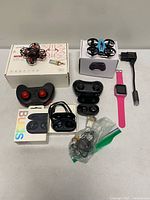Overview of all items: two drones, two controllers, smartwatch, two earbud cases, cables and batteries