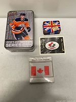 Front view of four main items including Upper Deck tin, Union Jack Paddington tin, sealed Canada patch, and packaged flag hand warmer